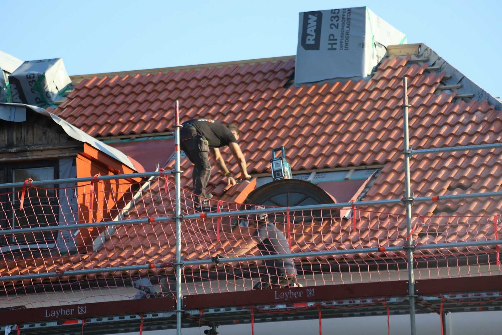 Couvreur au travail sur une toiture en tuiles, protégé par un échafaudage